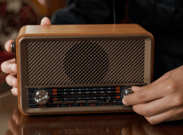 A person adjusting an old fashioned wooden radio on a reflective table top with ornate furniture in the background.