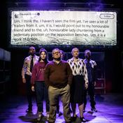 Cast members stand in a triangular formation, a tweet by Damian Green is projected above them.