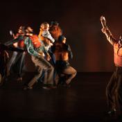 A group of people dart in different directions, wearing life vests. One man stands on his own with both arms raised above his head, his mouth is open as if he's yelling out.