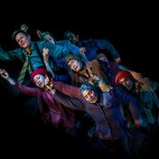 A group of people huddled together all outstretch their right arms.