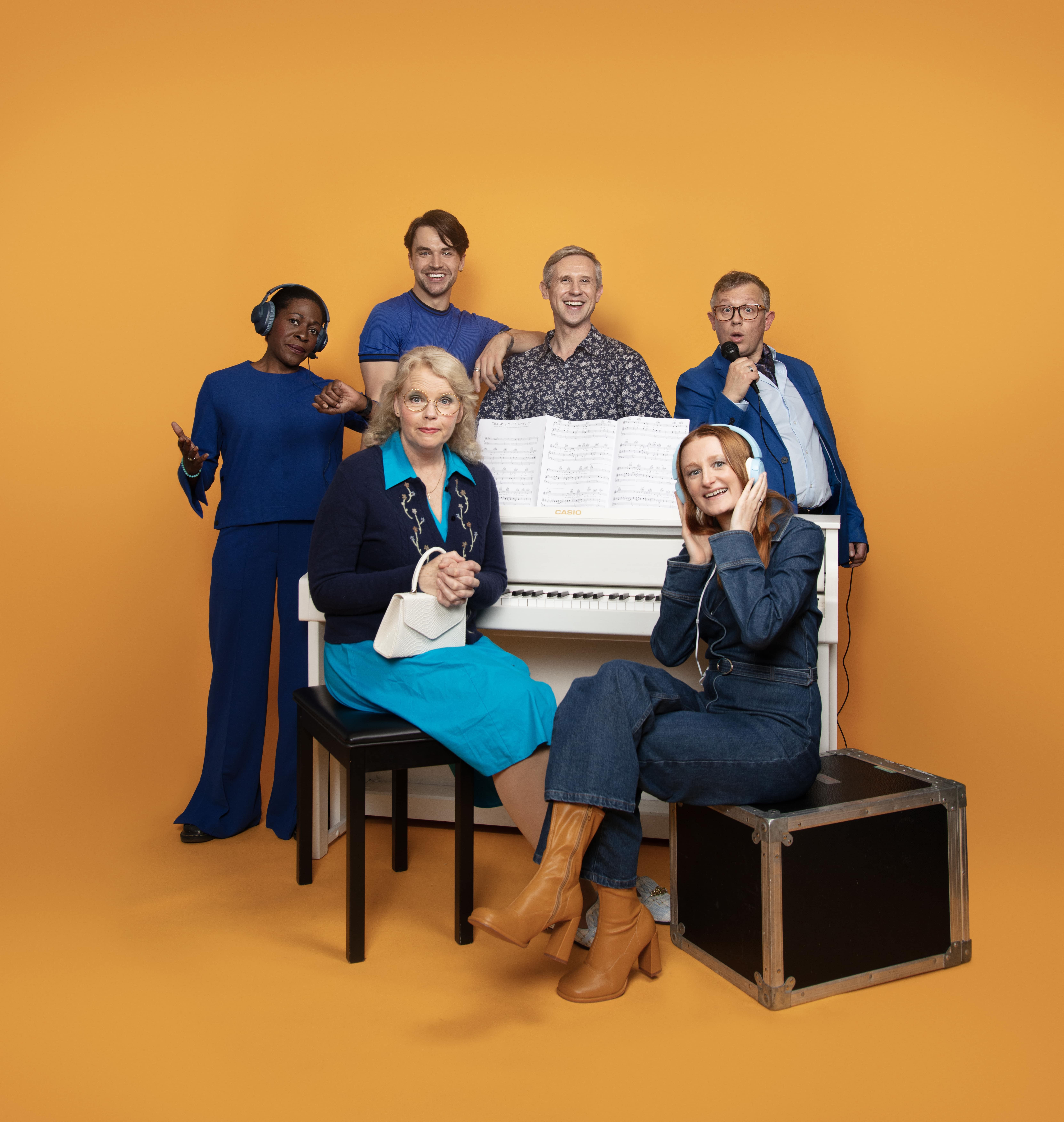 The cast of The Way Old Friends Do around a piano on a bright yellow background.