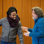 A man with his hand on his hip smiles at another man as they converse.