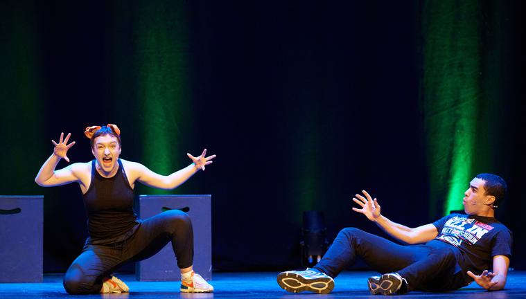 A woman crouches on the ground with her hands outstretched, she wears animal ears on her head. A man lies on the ground next to her, he looks shocked.