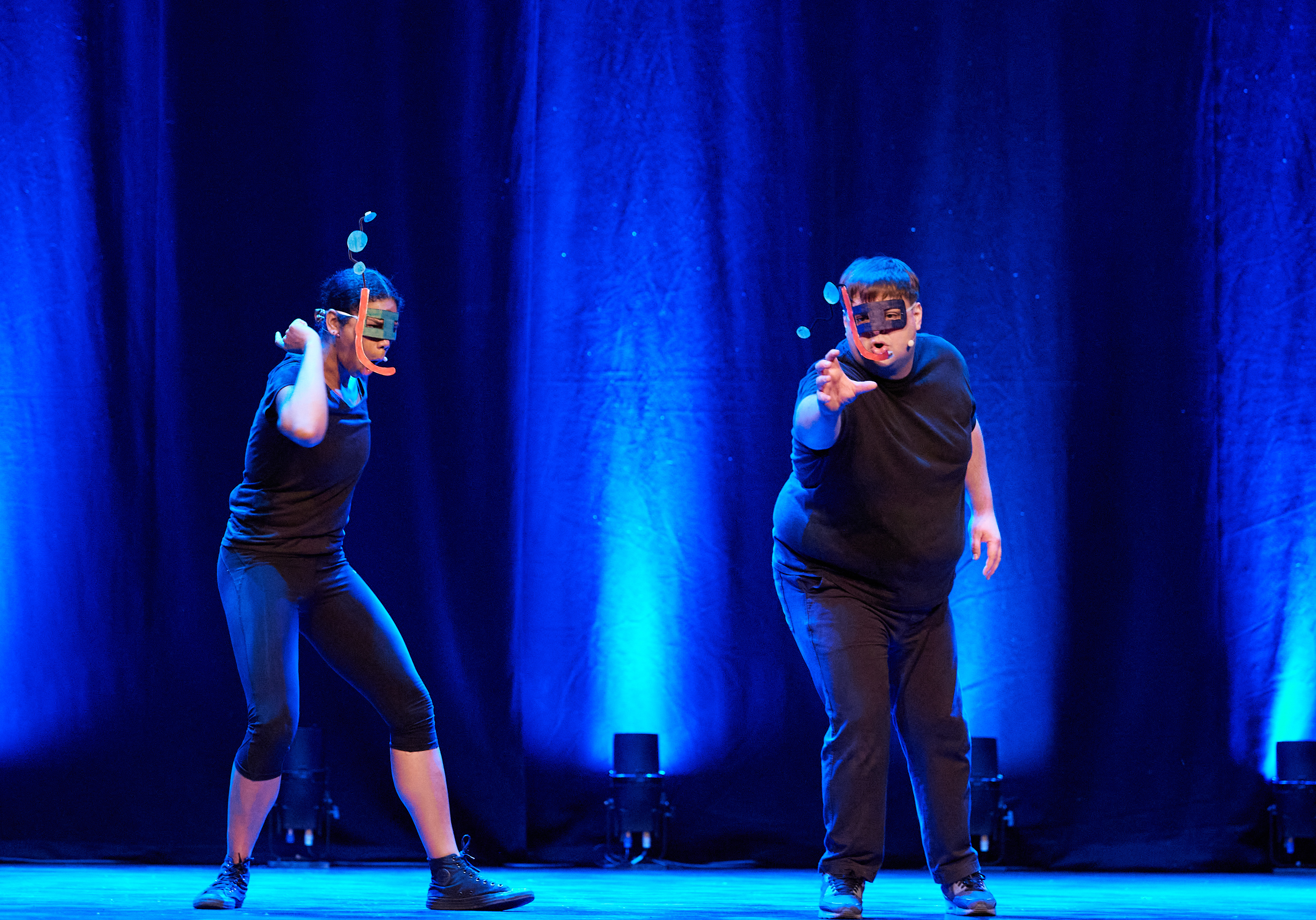 Two actors stand on stage, pretending they are scuba diving. They both wear makeshift snorkels with cardboard bubbles coming out of the top. The stage is lit up in bright blue.