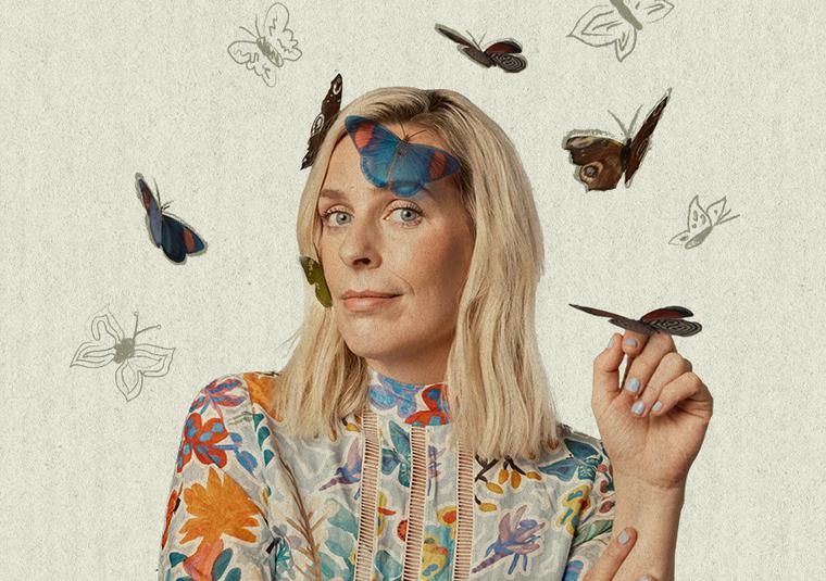 Sarah Pascoe is looking at the camera smiling, her head is surrounded by butterflies. A butterfly is resting on her lifted hand.