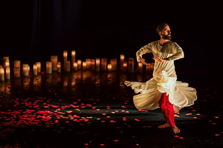A man dances on stage. It is lit with candles, and rose petals are scattered across the ground.