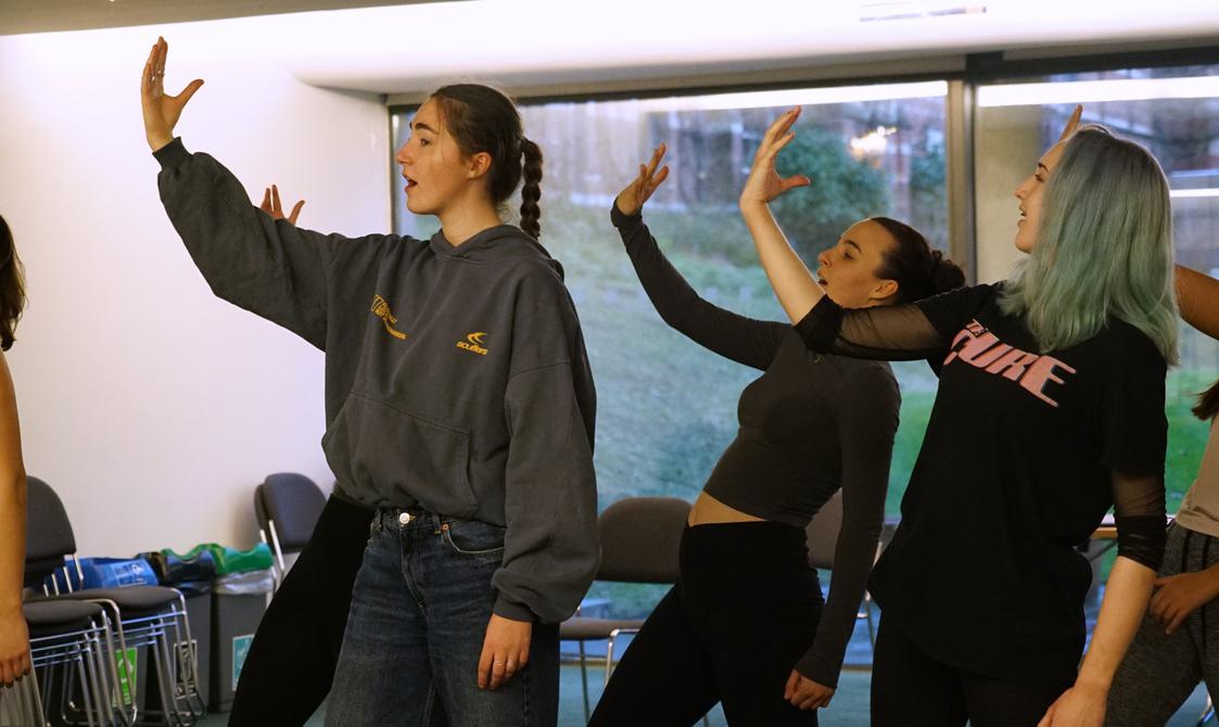 A group of three people can be seen raising their arms up above, they all look towards it as they lean back.