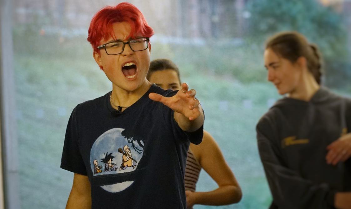 A person seems to yell, with their mouth wide and holds a hand out in front of them.