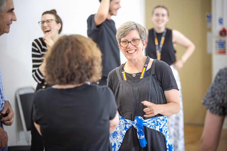 A group of actors with members of Oxford Playhouse staff during a rehearsal break. The actors are smiling, talking or laughing to one another.