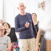 A group of actors standing looking at the actor standing immediately in front of the camera with looks of shock or surprise.