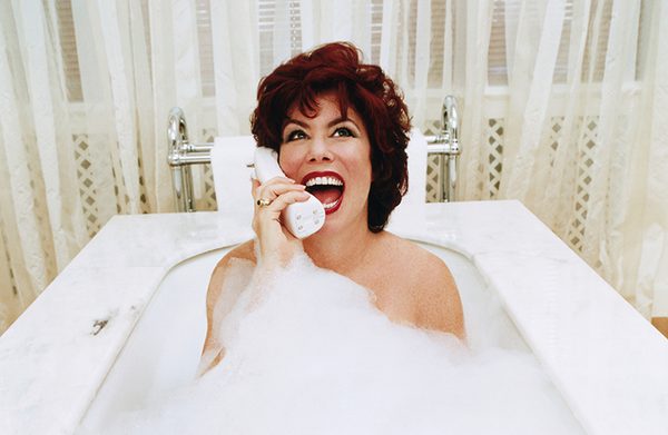 Ruby Wax sits in a bubble bath, head back and mouth wide open, talking on a wireless landline phone.