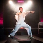 Joz Norris in a white track suit striking a pose on stage.
