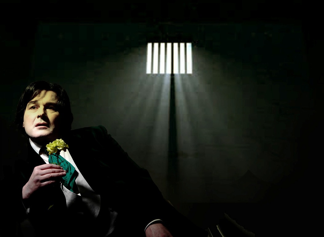 Gerard Logan as Oscar Wilde holding a flower in a prison cell.