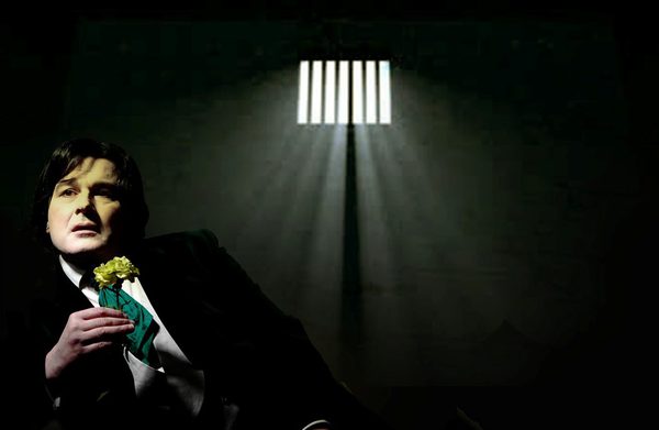 Gerard Logan as Oscar Wilde holding a flower in a prison cell.