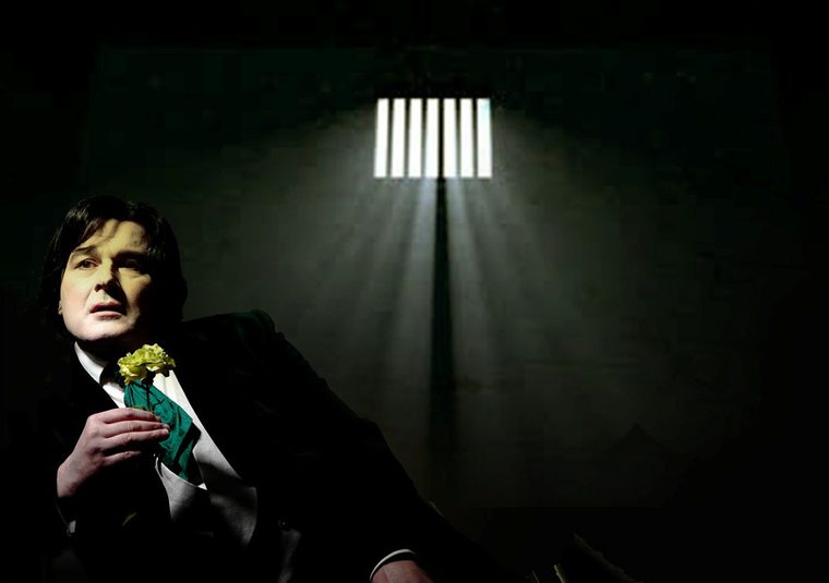 Gerard Logan as Oscar Wilde holding a flower in a prison cell.