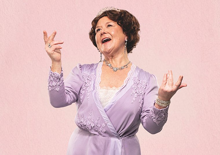 Actress in period costume in a light purple empire waist dress, adorned with jewels, singing with her arms up.