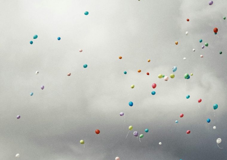 Hundreds of brightly coloured balloons against dark, stormy clouds.