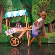 Matthew Morrell dressed in a bear costume pulling a food cart against a whimsical forest backdrop.