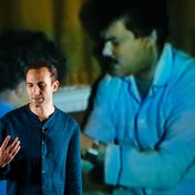 Khalid Abdalla on stage with a projection of an older gentleman and young boy.