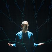 Khalid Abdalla on stage with projections of connecting lines covering him.