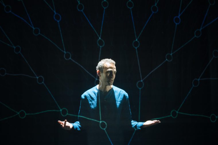 Khalid Abdalla on stage with projections of connecting lines covering him.