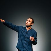 Khalid Abdalla on stage speaking to the audience with a grey backdrop.