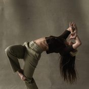 Dancer in muted green top and brown trousers in a modern dance pose.