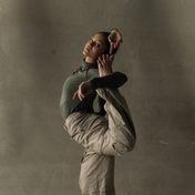Dancer in muted green top and brown trousers in a modern dance pose.