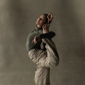 Dancer in muted green top and brown trousers in a modern dance pose.
