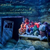 The cast of The Beekeeper of Aleppo in a boat with lifejackets with projections of the sea.