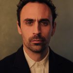 Alex Mugnaioni profile image against a brown-orange background.