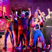 A group of actors cheering on stage in a group with silly expressions on their face.