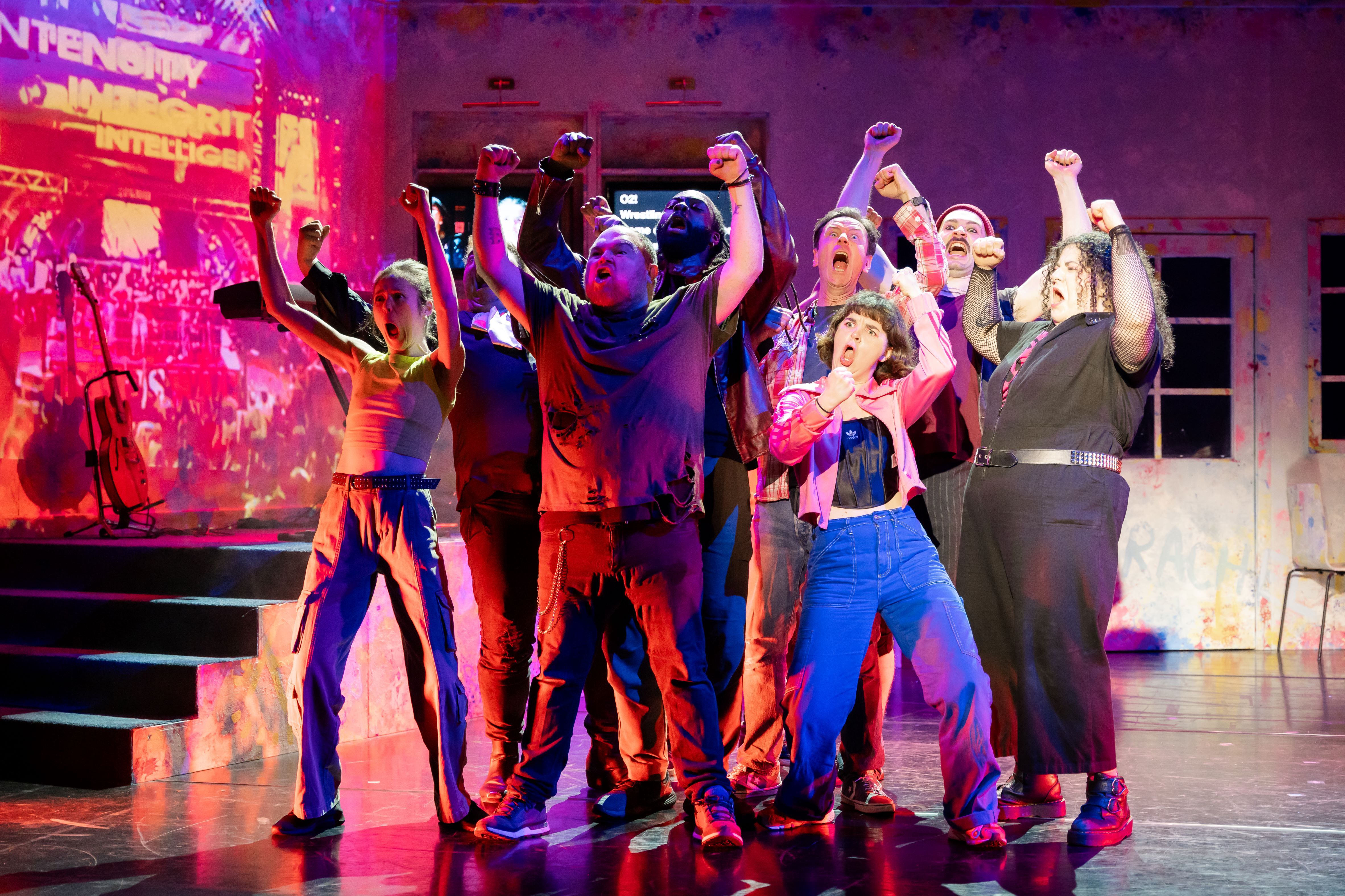 A group of actors cheering on stage in a group with silly expressions on their face.