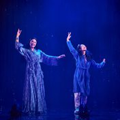 A mother and daughter on stage dancing together in bath robes, laughing.