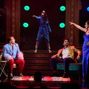An emotionally tense scene as Frankie, as an adult, points towards a light while the younger version of herself also points towards a light. Two figures in suits sitting down look at her, appalled.