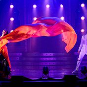 A dramatic scene as two actors are singing passionately with dramatic lighting and the actress' sari blowing dramatically across the stage.