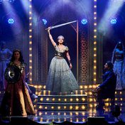 A dramatic scene of Frankie in a glamourous costume holding up a sword with spotlights directly on her.