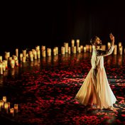 Dancer in traditional white dress dancing inside a circle of lit candles with rose petals across the floor.