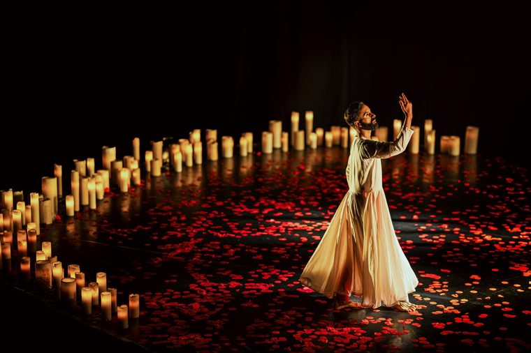 Dancer in traditional white dress dancing inside a circle of lit candles with rose petals across the floor.