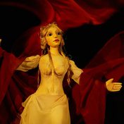 Venus in a white flowy dress with red fabric swirling around her. Puppet design inspired by Japanese Bunraku puppets and the Jacobean Court Masque.