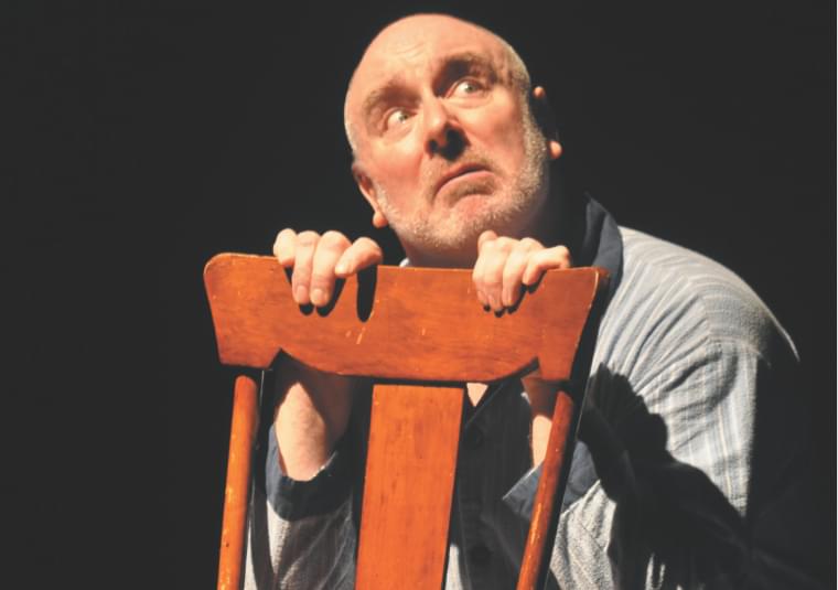Image of Guy Masterson peering over the back of a wooden chair looking sideways