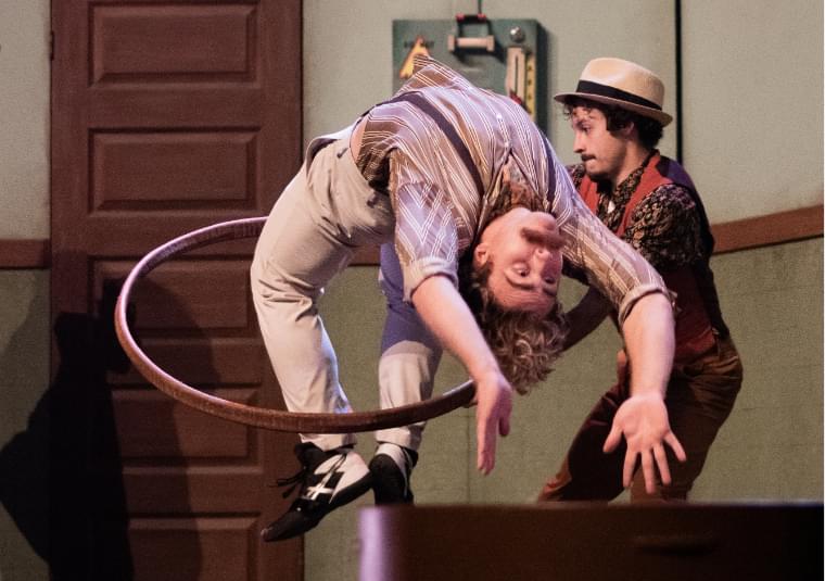 A man is back flipping through a hoop which is being held by another man.