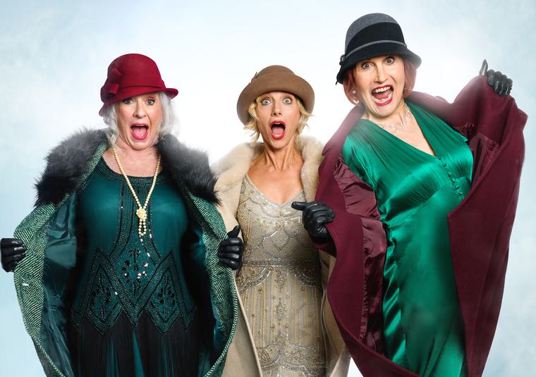 Three woman open up their coats to reveal flapper inspired gowns. They all wear hats and pose with their mouths open.