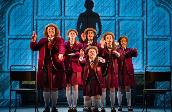 Group of actors on stage dressed in school uniform performing a salute