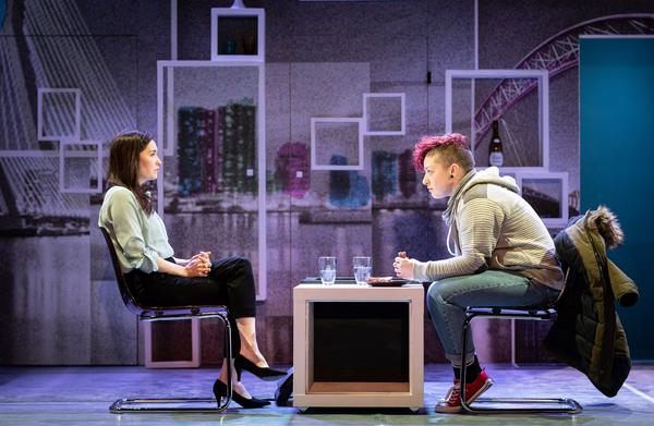 Two people sit on chairs opposite one another. One is eating a sandwich.
