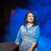 A woman stands on stage holding onto a black pram