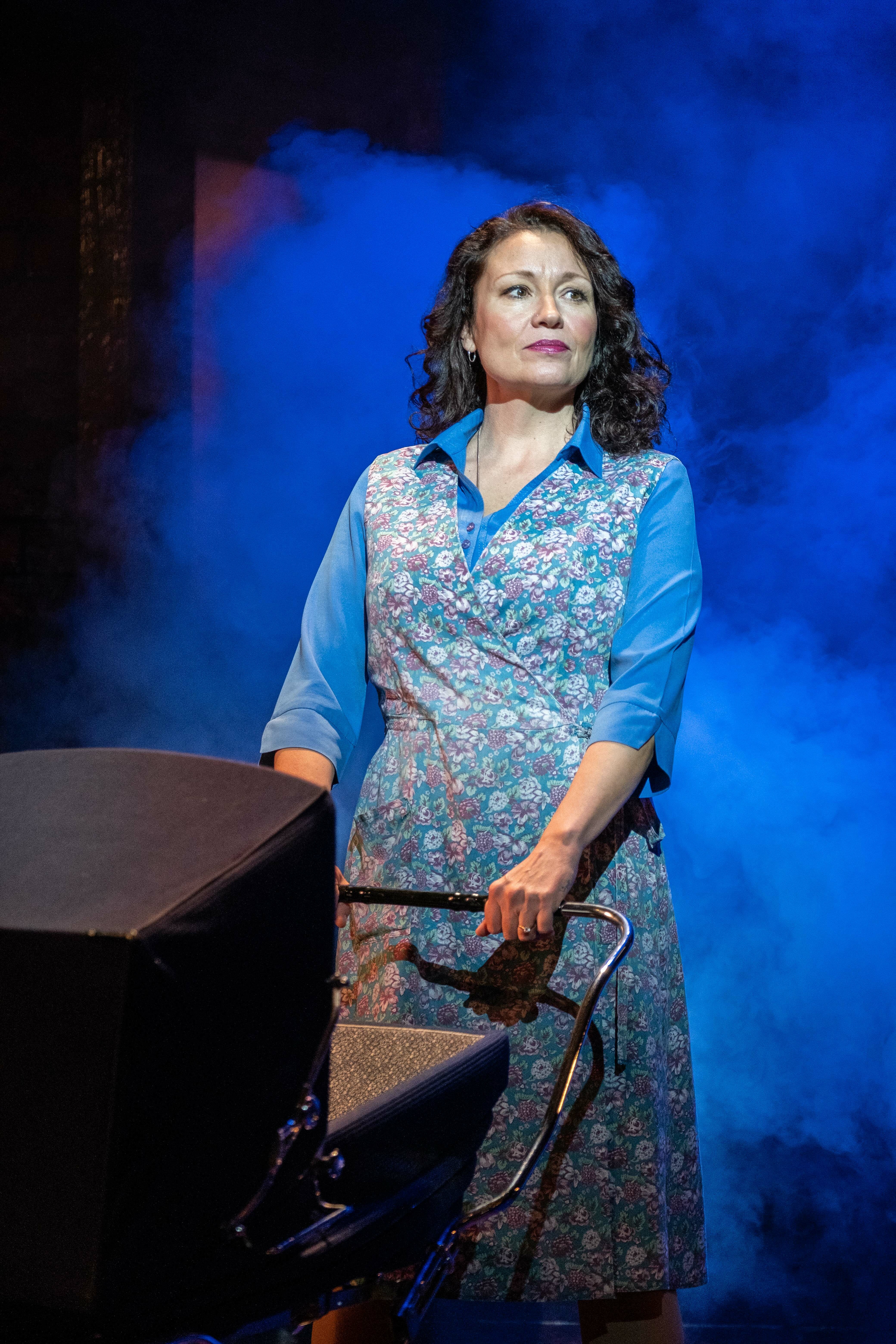 A woman stands on stage holding onto a black pram