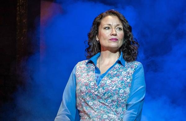 A woman stands on stage holding onto a black pram