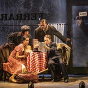 Four people sit around a table, one man looks through the glass door from outside.