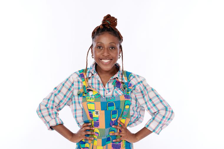 Dumile Sibanda was her hands on her hips, smiling. She wears a plaid shirt with mobile phone patterned overalls on top.